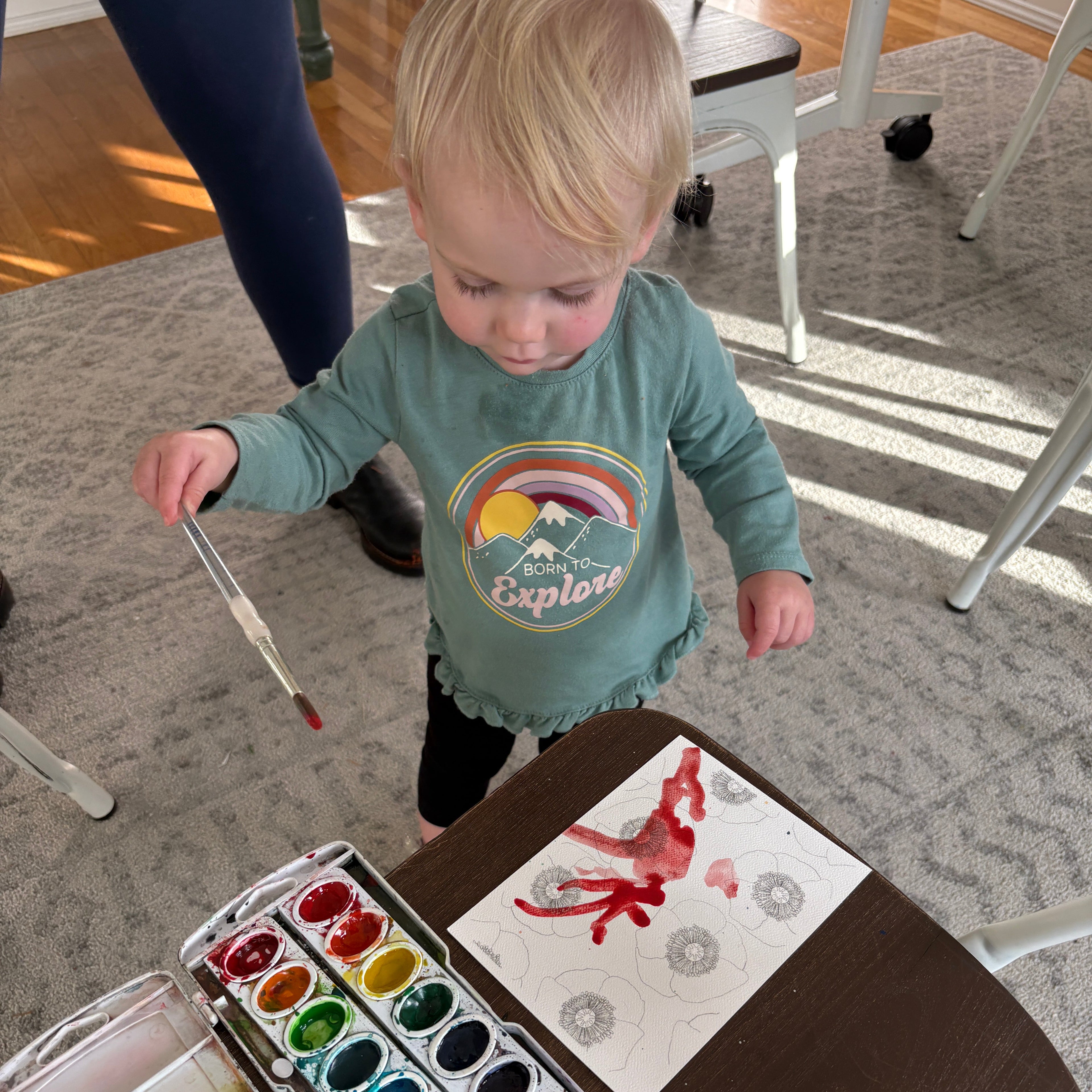 Child painting on a piece of paper with watercolors at a table.